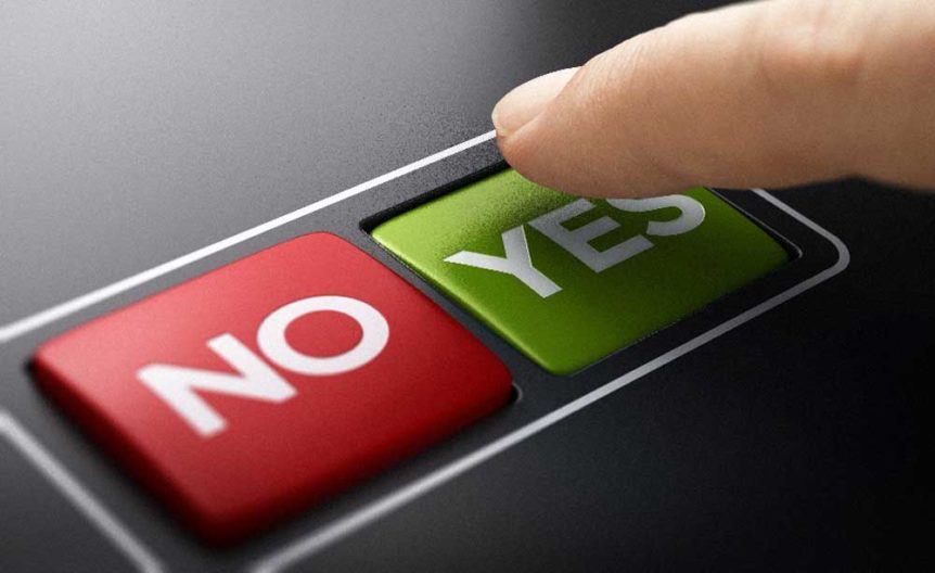 Close up of two rectangular side-by-side buttons. One red button with the word no, next to a green button that says yes. An index finger has just pressed the yes button.
